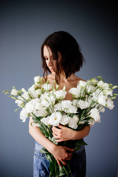 Portrait of a beautiful girl with dark hair with a huge bouquet of white and pink lisianthus. - Zdjęcie, obraz