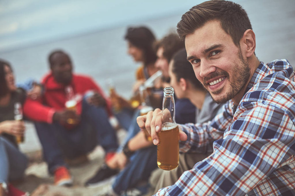 Happy man sitting near his friends at the seaside - Фото, изображение