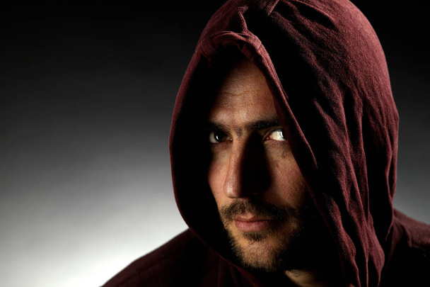 portrét pohledného neholého muže v tmavě červeném kapuci na šedém pozadí  - Fotografie, Obrázek