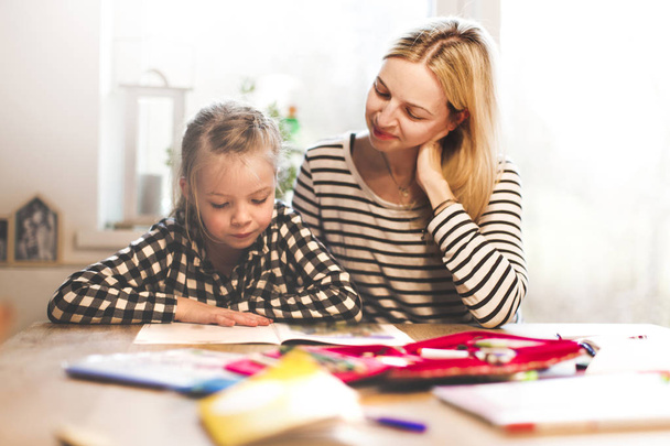 mother and daughter togehter doing schoolwork while sitting at table in home - Foto, Bild
