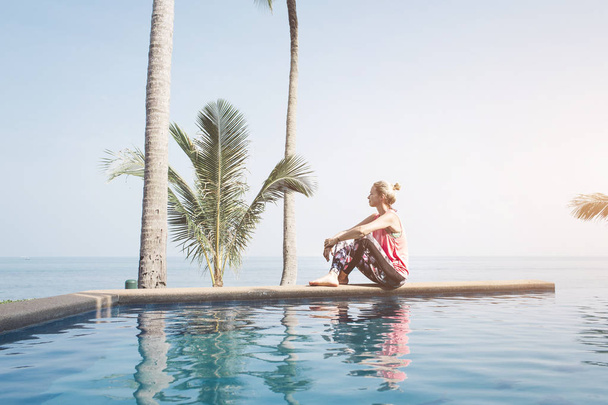 Caucasian woman looking to ocean while sitting on pool  - Foto, Bild