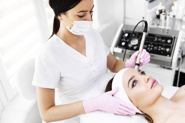 A woman came to laser hair removal facial. The woman lies and smiles, the doctor leads him in the face with a modern laser epilator. They are in the modern clinic.close up - Photo, Image