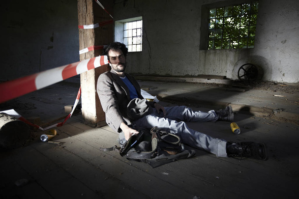 drunkard bearded man leaning on wooden beam while sitting in neglected building  - Fotografie, Obrázek