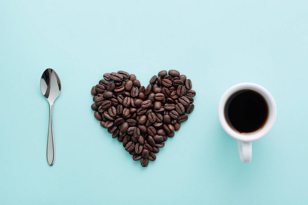 Чашка кави, форма серця кавових зерен та чайна ложка на синьому фоні. Плоский, креативний дизайн. Я люблю концепцію кави
. - Фото, зображення