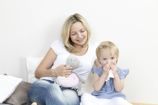 sick child blowing in handkerchief while sitting near mother at home  - Foto, immagini