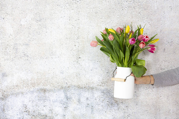 female hand holding flower vase with colorful tulips on grey wall background  - Φωτογραφία, εικόνα