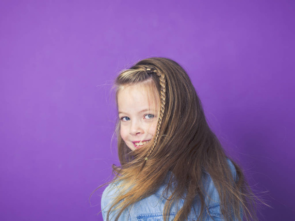 portrait of cute little girl wearing blue denim shirt in front of violet background in studio - Foto, imagen