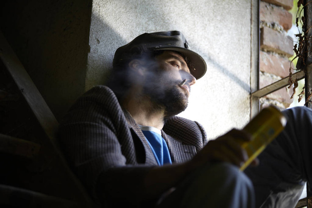 bearded homeless man smoking cigarette and sitting near window  - Fotografie, Obrázek