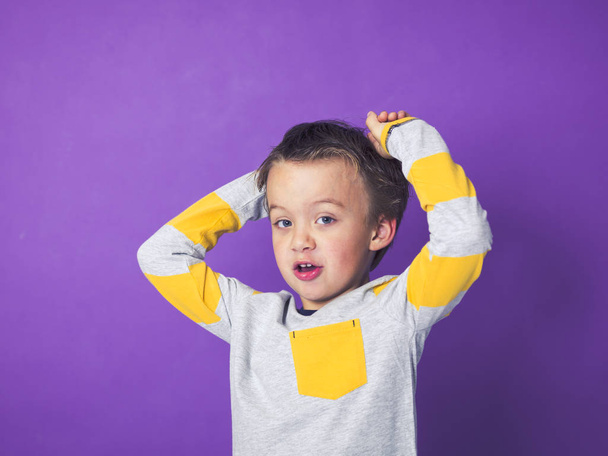 happy little boy having fun while posing in front of violet background - 写真・画像