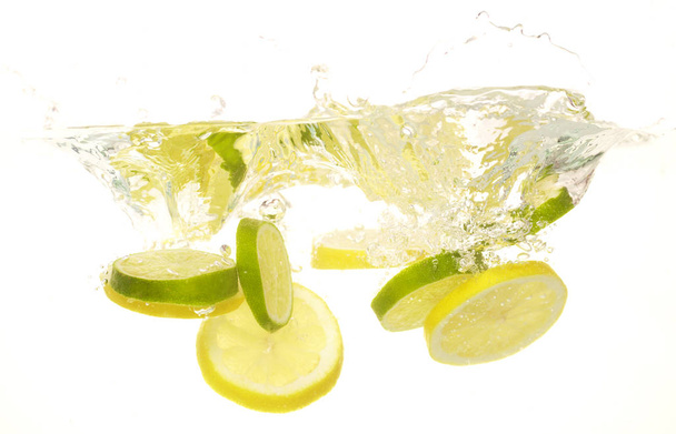 спелые ломтики лимона и лайма падают на воду, крупным планом
   - Фото, изображение