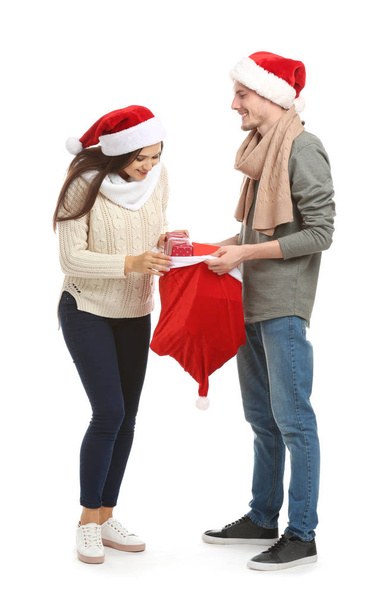 Young woman choosing gift from Christmas bag held by her husband on white background - Foto, immagini