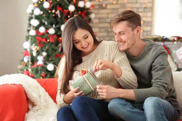 Χαριτωμένο νεαρό ζευγάρι με το δώρο Χριστουγέννων στο σπίτι - Φωτογραφία, εικόνα