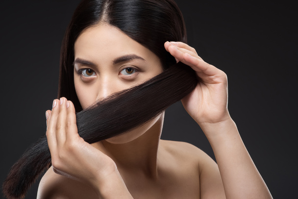 портрет красивой азиатской женщины со здоровыми и сильными волосами, изолированными на черном
 - Фото, изображение