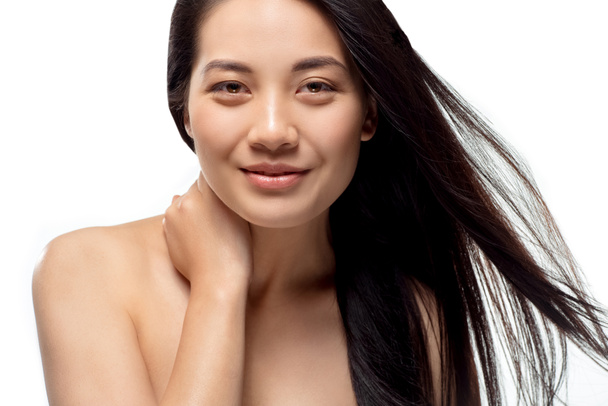 retrato de sonriente modelo asiático con el pelo fuerte y saludable mirando a la cámara aislada en blanco
 - Foto, Imagen