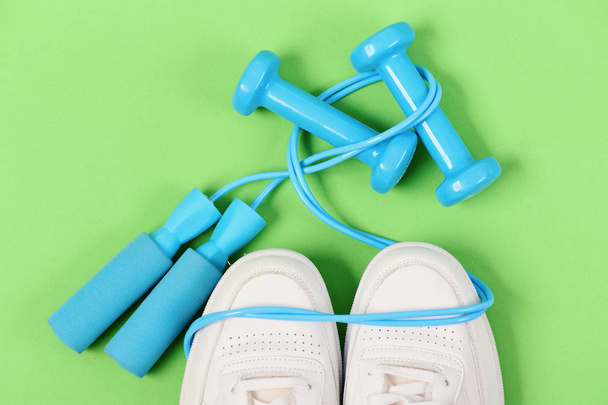 Dumbbells in cyan blue color on white trainers, top view - Photo, image