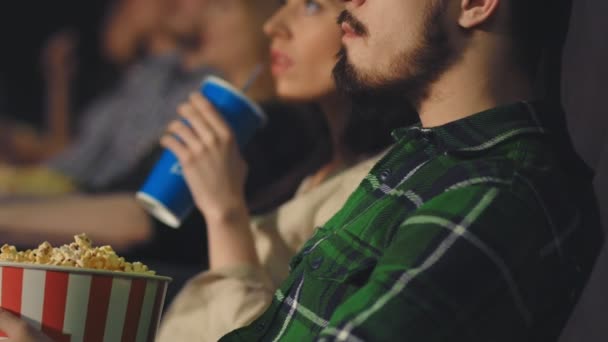 A young guy with a beard eats popcorn in the cinema - Záběry, video