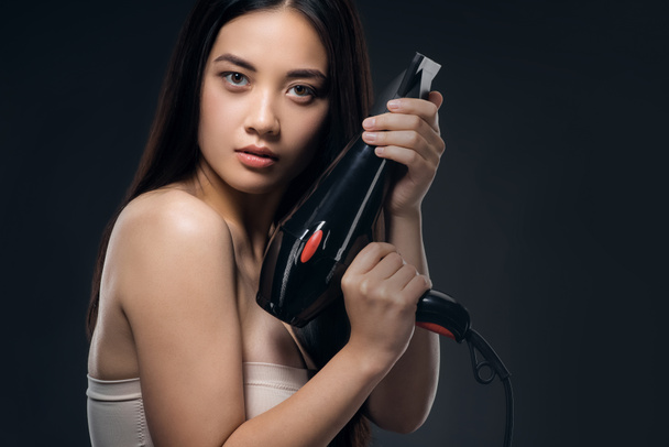 retrato de mujer asiática con secador de pelo mirando a la cámara aislada en negro
 - Foto, Imagen