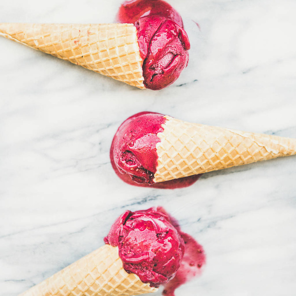 Melting natural raspberry sorbet ice-cream scoops in sweet waffle cones over light marble background - Zdjęcie, obraz