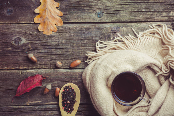Осіння композиція, осіннє листя, жолуді, скляна чашка чаю та теплий шарф на старому дерев'яному столі
. - Фото, зображення
