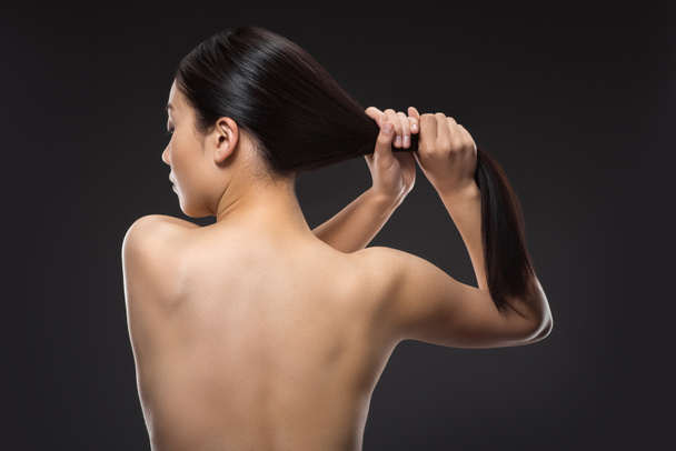 Rückseite der hemdlosen Frau mit schönem, glänzendem Haar isoliert auf schwarz - Foto, Bild