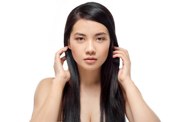 портрет молодої азіатської моделі зі здоровим і блискучим волоссям дивиться на камеру ізольовано на білому
 - Фото, зображення