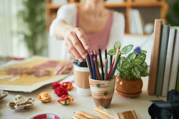 Δημιουργική γυναίκα λαμβάνοντας χρωματιστό μολύβι από τον κάτοχο ενώ κάθεται στο ξύλινο τραπέζι και καθιστώντας βοτανολόγιο διακόσμηση - Φωτογραφία, εικόνα