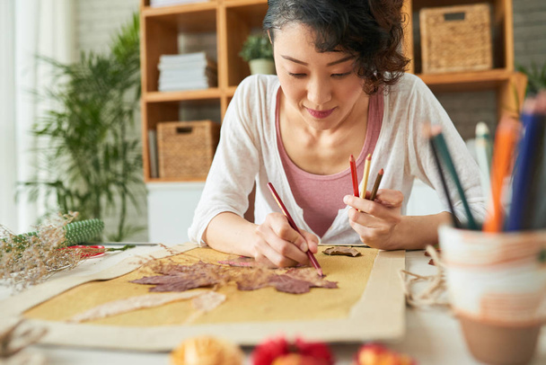 asian designer woman sitting at wooden table and making herbarium decor art picture  - Photo, Image