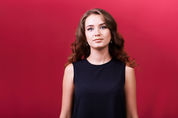 Studio portrait of a young cute attractive girl with brunette curly hair on red background. - Foto, Imagen