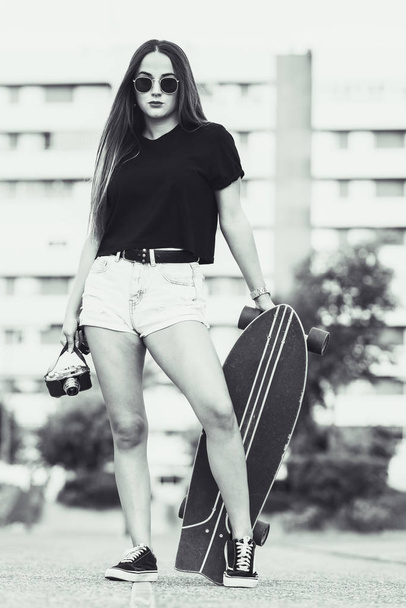 Mooie jonge vrouw poseren met retro camera en skate - Foto, afbeelding