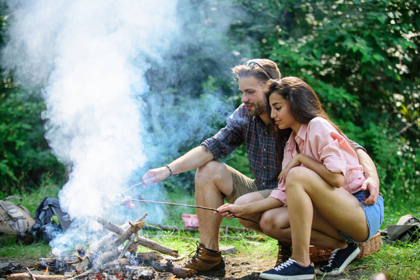 Couple roasting sausages on sticks nature background. Traditional roasted food as attribute of picnic. Camping and picnic. Couple in love enjoy camping forest roasting sausage at bonfire - Photo, Image