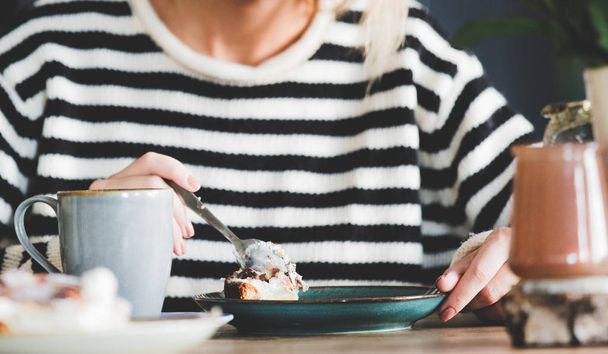 Jeune femme avec une tasse de café ou de thé et gâteau assis dans une chaise à la cuisine à l'heure du petit déjeuner. Intérieur de style hollandais
. - Photo, image