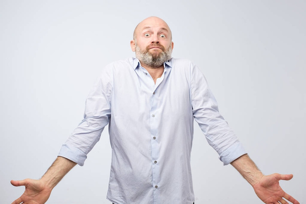 Confused mature bearded man standing and shrugging shoulders isolated over white background. I do not know the solution of this problem concept - Photo, Image