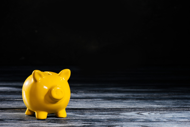 close-up view of yellow piggy bank on wooden table on black - 写真・画像