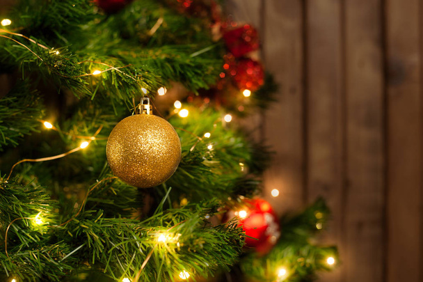 Golden Christmas ball on a Christmas tree with a garland on the background of a wooden wall - Foto, Bild