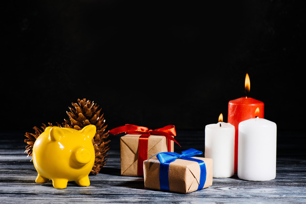 sárga malacka bank, fenyőtobozok, karácsonyi ajándékokat és égő gyertyák - Fotó, kép