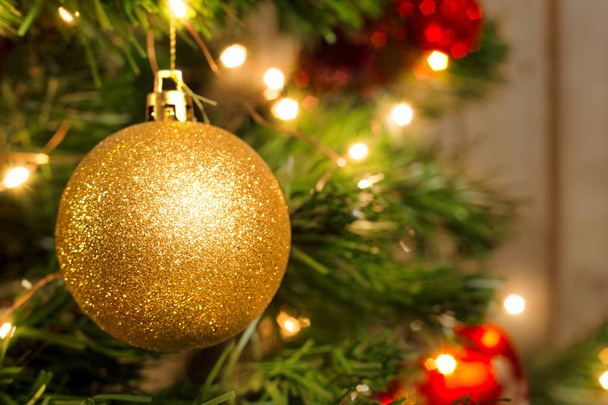 Golden Christmas ball on a Christmas tree with a garland on the background of a wooden wall - Foto, Imagen