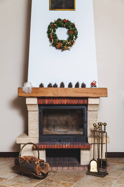 nowoczesny kominek ozdobione Boże Narodzenie wieniec i posąg Świętego Mikołaja. Przed kominkiem jest kute drovnitsa i zestaw mosiądz narzędzia - Zdjęcie, obraz