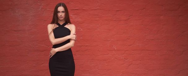 fashionable pretty woman is wearing black dress over red brick wall. Outdoors portrait - Foto, imagen