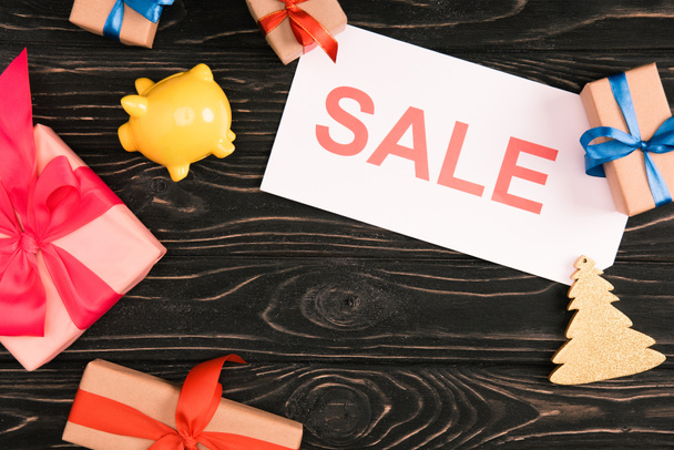 top view of sale sign, yellow piggy bank and christmas presents on wooden surface - 写真・画像