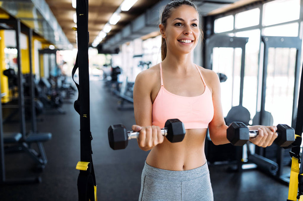 Young beautiful woman doing exercise with dumbbell in gym - Photo, Image