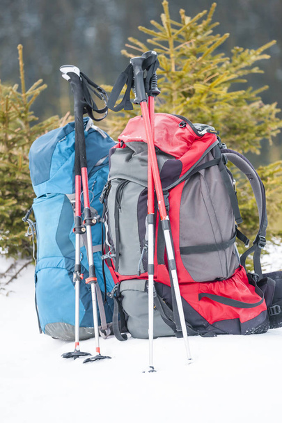 Zwei Rucksäcke im Hintergrund von schneebedeckten Bergen und blauem Himmel. Ein Rucksack im Schnee. Aktiver Lebensstil. Wandern im Winter. Ausrüstung zum Wandern. Trekkingstöcke. - Foto, Bild