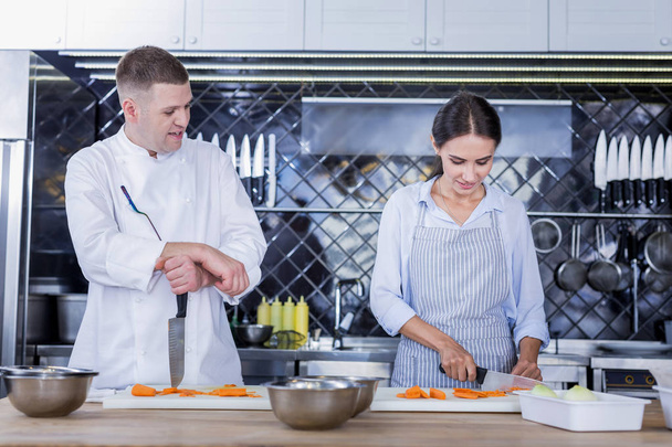 Young lady cooking a tasty dish with a chef - Foto, afbeelding