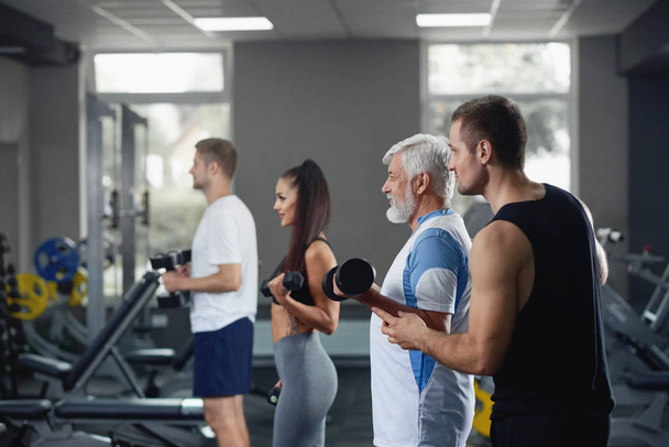 Elderly man doing exercise with group of younger people at gym. - Foto, imagen