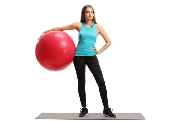 Full length portrait of a young female with a pilates ball standing on an exercise mat isolated on white background - Φωτογραφία, εικόνα