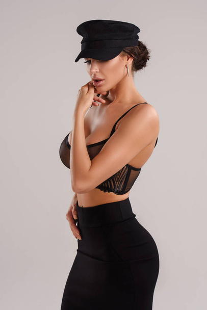 sexy young beautiful brunette woman posing in studio wearing black hat, skirt and bra  - Photo, image