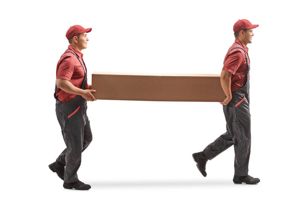 Full length profile shot of two movers carrying a big cardboard box isolated on white background - Fotoğraf, Görsel