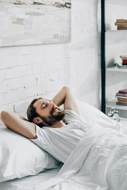 smiling young bearded man waking up in bedroom at home  - Foto, imagen