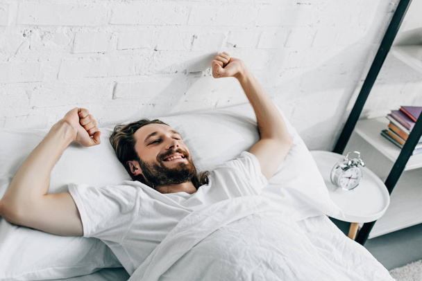 happy bearded man doing stretch in bed during morning time at home  - Photo, Image