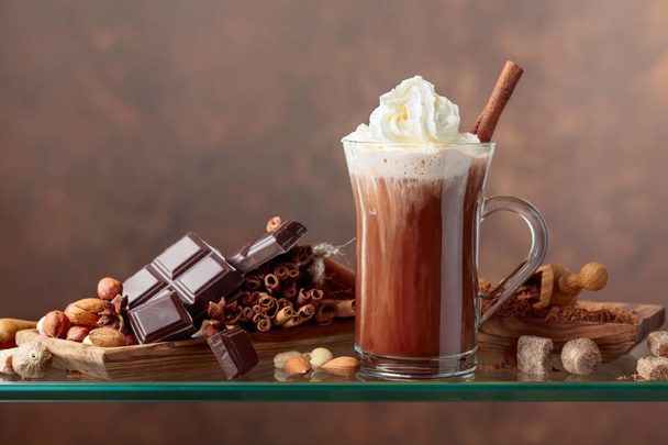 Cocoa with cream, cinnamon, chocolate pieces and various spices on a brown background. Copy space for your text. - Φωτογραφία, εικόνα