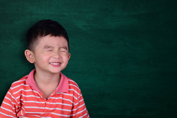 Happy Asian kid smiling on empty green chalkboard with copy space for add text or word, education and back to school concept idea. - Photo, image